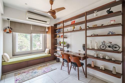 Study nook with window seat, wooden desk, and shelving filled with decorative objects
