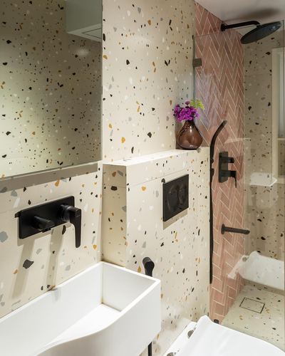 Bathroom with speckled terrazzo walls, black fixtures, and pink herringbone tile shower area
