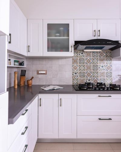 White L-shaped kitchen with grey countertop, patterned tile backsplash behind gas hob and chimney hood