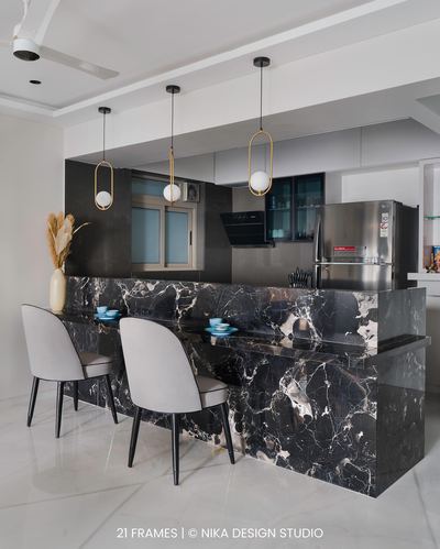 Kitchen island in black marble with pendant lights and grey bar chairs in modern Mumbai home