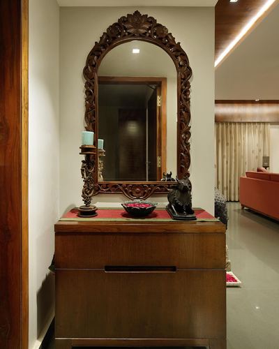 Carved wooden arched mirror above console table with candle stand and figurines in a foyer
