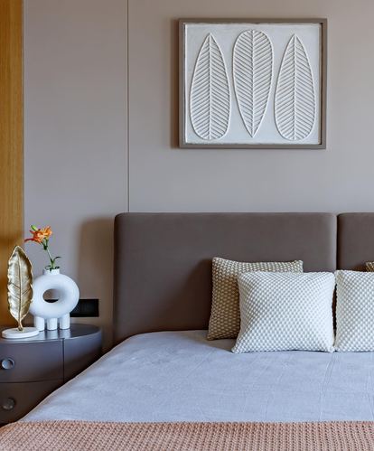 Nude-toned bedroom with upholstered headboard, patterned cushions, and a textured leaf relief art panel above.
