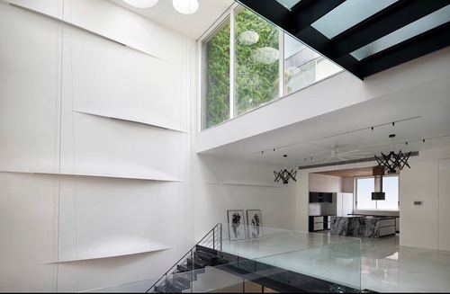 Double-height white interior with floating shelves, glass floor bridge, and kitchen beyond skylight