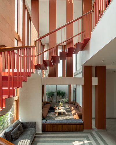 Double-height living space with red cantilevered staircase above a sunken brown sofa seating area
