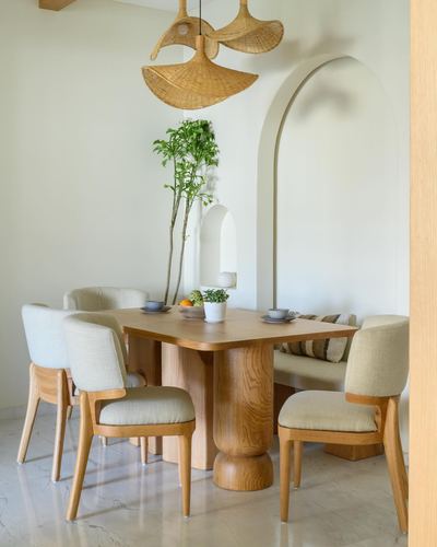 Dining table with sculptural wood pedestal base, upholstered chairs, arched wall niche, and woven pendant light
