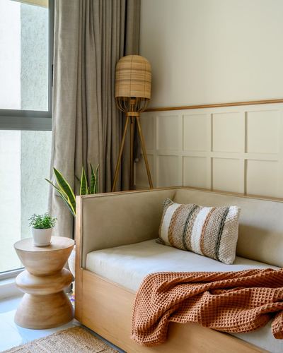 Beige upholstered daybed corner with wood side table, tripod lamp, and terracotta throw