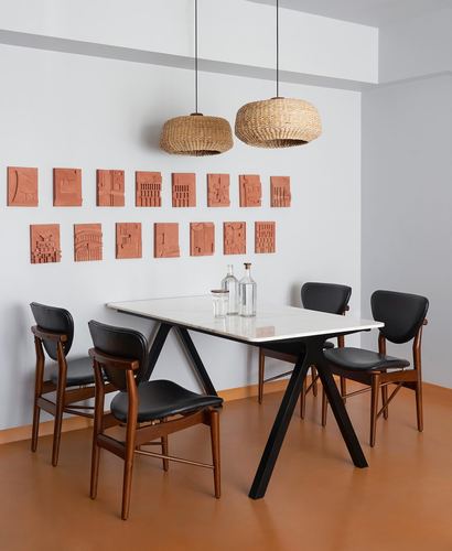 Dining table with stone top and black angled legs under woven pendant lights, terracotta wall art above