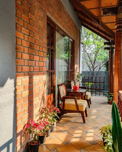 Covered brick veranda with wooden furniture and potted plants overlooking green trees