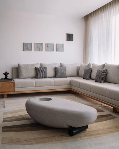 Beige L-shaped sofa with striped cushions, oval stone coffee table, sheer curtain, framed art above
