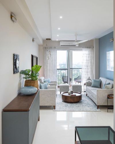 Living room with grey sofas, round wood coffee table, sheer-curtained balcony beyond