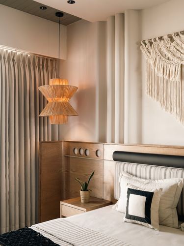 Bedroom corner with woven pendant light, wood headboard wall, and macrame hanging above bed