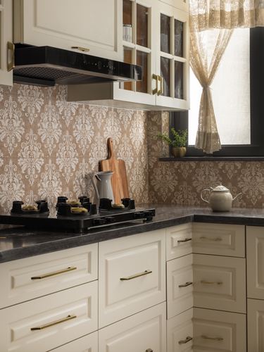 Kitchen corner with patterned backsplash, cream cabinets, black stove and countertop, curtained window