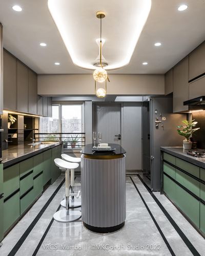 Mumbai kitchen with sage green cabinetry, black countertops, and a fluted round central island under pendant lights
