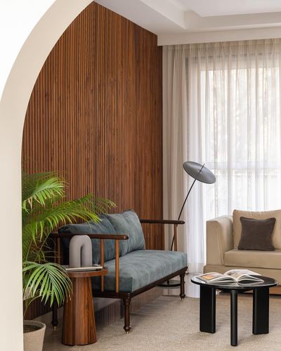 Living room with arched fluted wood wall, teal sofa, black side tables, sheer curtains
