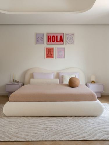 Bedroom with curved cream boucle bed, blush bedding, lavender nightstands and colorful framed art above