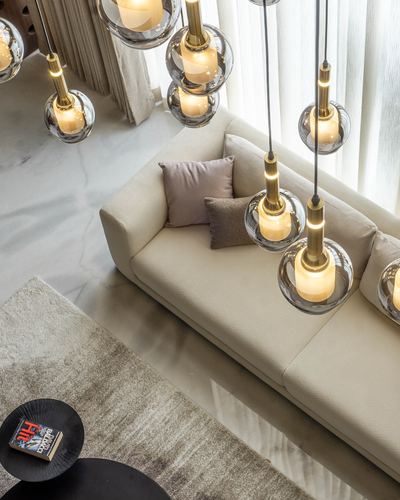 Overhead view of cream sofa beneath cascading brass and glass globe pendant lights on marble floor