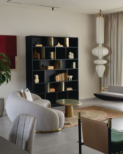 Living room with black brass-trimmed bookshelf, boucle swivel chairs, and sculptural pendant lamp near curtained window