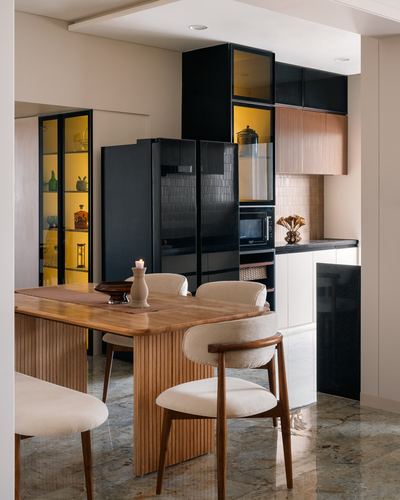 Dining table with fluted wood chairs beside a black kitchen with glowing backlit cabinets