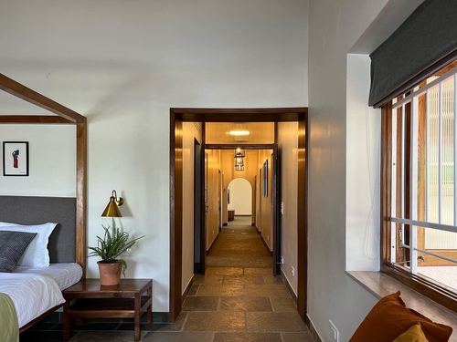 Bedroom with wood canopy bed opening onto a long lit corridor with arched doorways