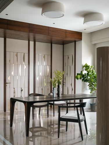 Dining table with sculptural chairs before patterned wooden doors and greenery