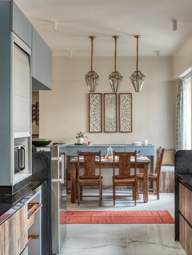 Dining area with carved wood panels, geometric pendants, wooden table and chairs on marble floor beside kitchen