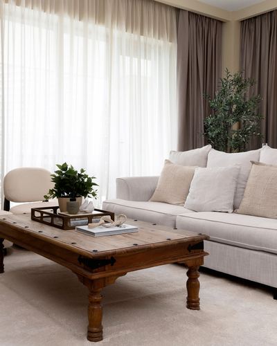 Neutral living room with linen sofa, studded wooden coffee table, and sheer curtains.