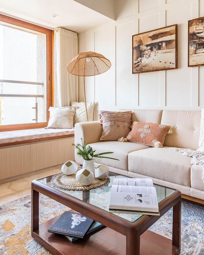 Living room corner with beige sofa, patterned cushions, rattan floor lamp, window seat and wooden coffee table