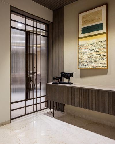 Entryway with fluted wood console, brass sculptures, framed art, and reeded glass door
