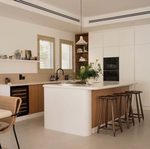 Modern kitchen with curved white and wood island, walnut stools, and shuttered windows