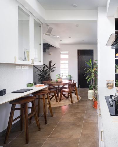White kitchen with wooden stools, breakfast counter, and round dining table with plants beyond