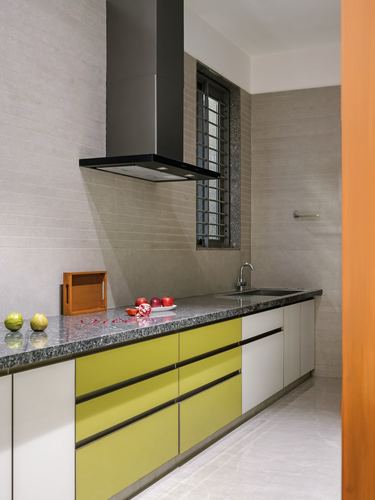 Modern galley kitchen with yellow and white cabinetry, black chimney hood, stone countertop.
