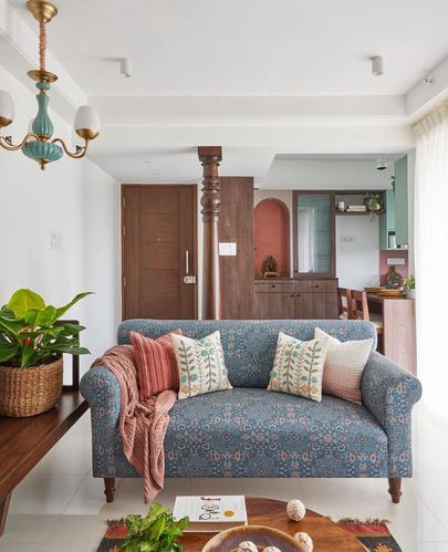 Living room with block-print sofa, turned wood column, and terracotta pooja niche beyond