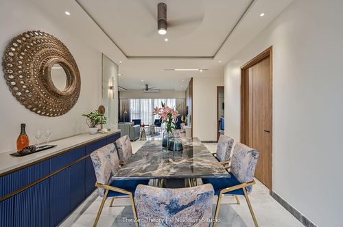 Dining area with marble table, navy upholstered chairs, and a large sunburst mirror above a blue console