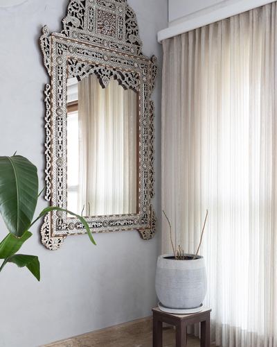 Mother-of-pearl inlaid mirror on grey wall beside sheer-curtained window and potted plant