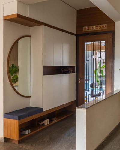 Foyer with round mirror, white and wood cabinetry, bench, and wooden door with metal grille