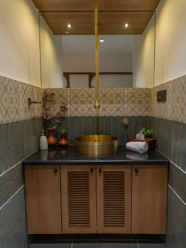 Bathroom vanity with brass vessel sink, dark stone counter, and louvered wood cabinetry