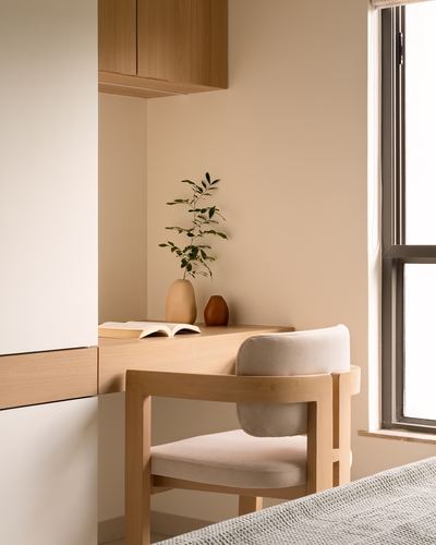 Wooden corner desk with cane chair, ceramic vases and plant beside a window in a beige study nook