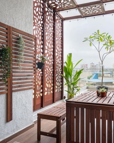 Balcony with wooden furniture, potted plants and laser-cut jali panels overlooking city skyline