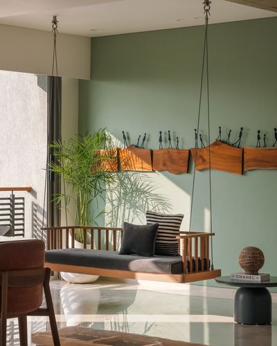 Wooden hanging daybed swing in sage green living room with wall art and palm