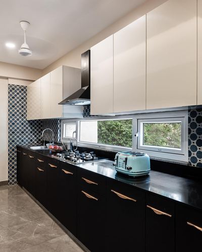 Galley kitchen with cream upper cabinets, black lower cabinets, patterned tile backsplash, and window over sink