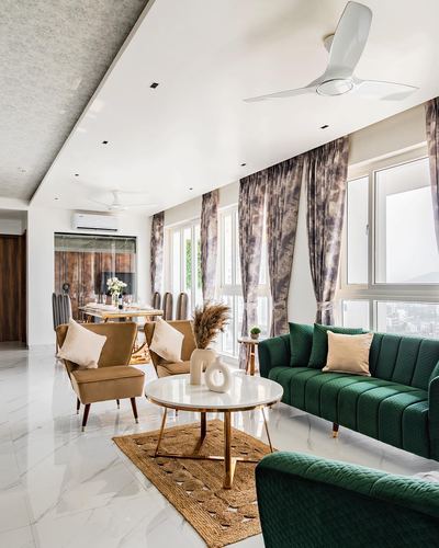 Living and dining space in Pune home with green velvet sofas, marble floor and coffee table, patterned curtains
