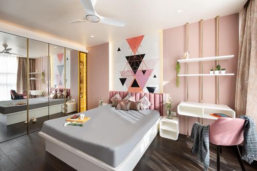 Pink bedroom with geometric mural, tufted headboard, mirrored wardrobe, and suspended shelving.