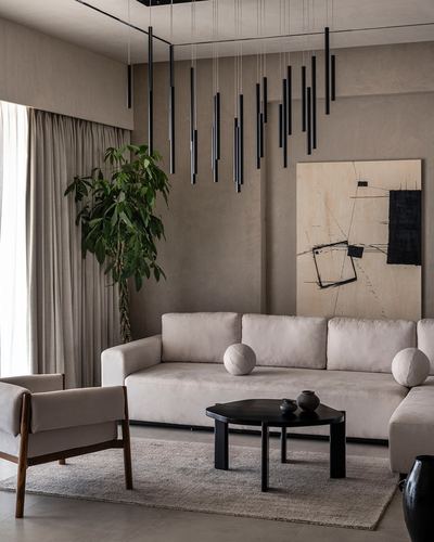 Minimalist beige living room with linear pendant cluster, cream sofa, black round coffee table