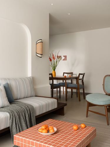 Living room with striped sofa, arched niche, terracotta tiled coffee table and dining nook beyond