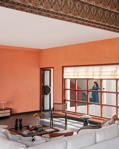 Terracotta living room with cane armchair, sunflower bouquet, and window framing a woman on the balcony
