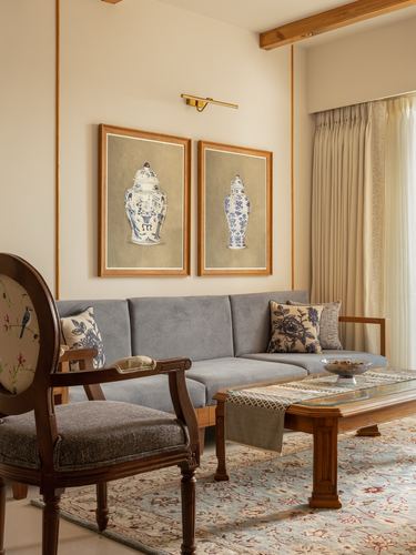 Living room with grey sofa, carved wooden armchair, and paired ginger jar prints on beige wall