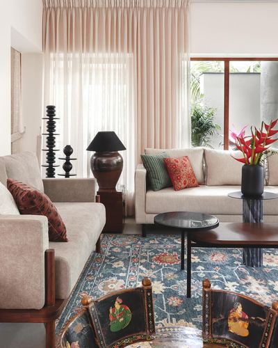 Living room with beige sofas, blue patterned rug, blush sheer curtains and painted wooden chairs in foreground
