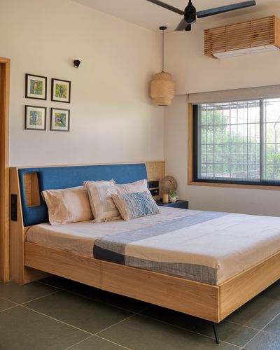 Wooden bed with blue upholstered headboard, cane pendant light, and framed bird prints in sunlit bedroom