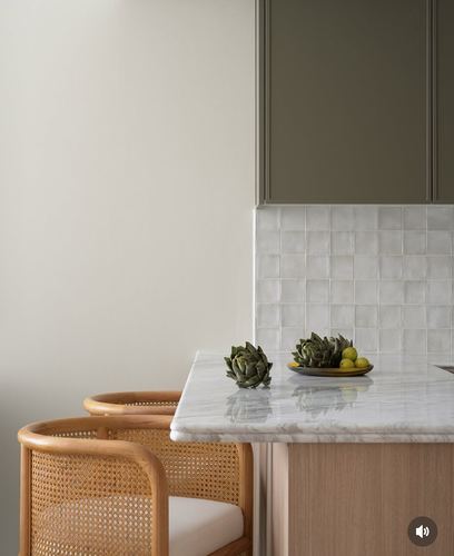 Kitchen island corner with marble countertop, cane stools, and tiled backsplash under olive cabinetry