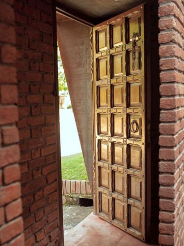 Open carved wooden door set in an exposed brick doorway leading to a garden